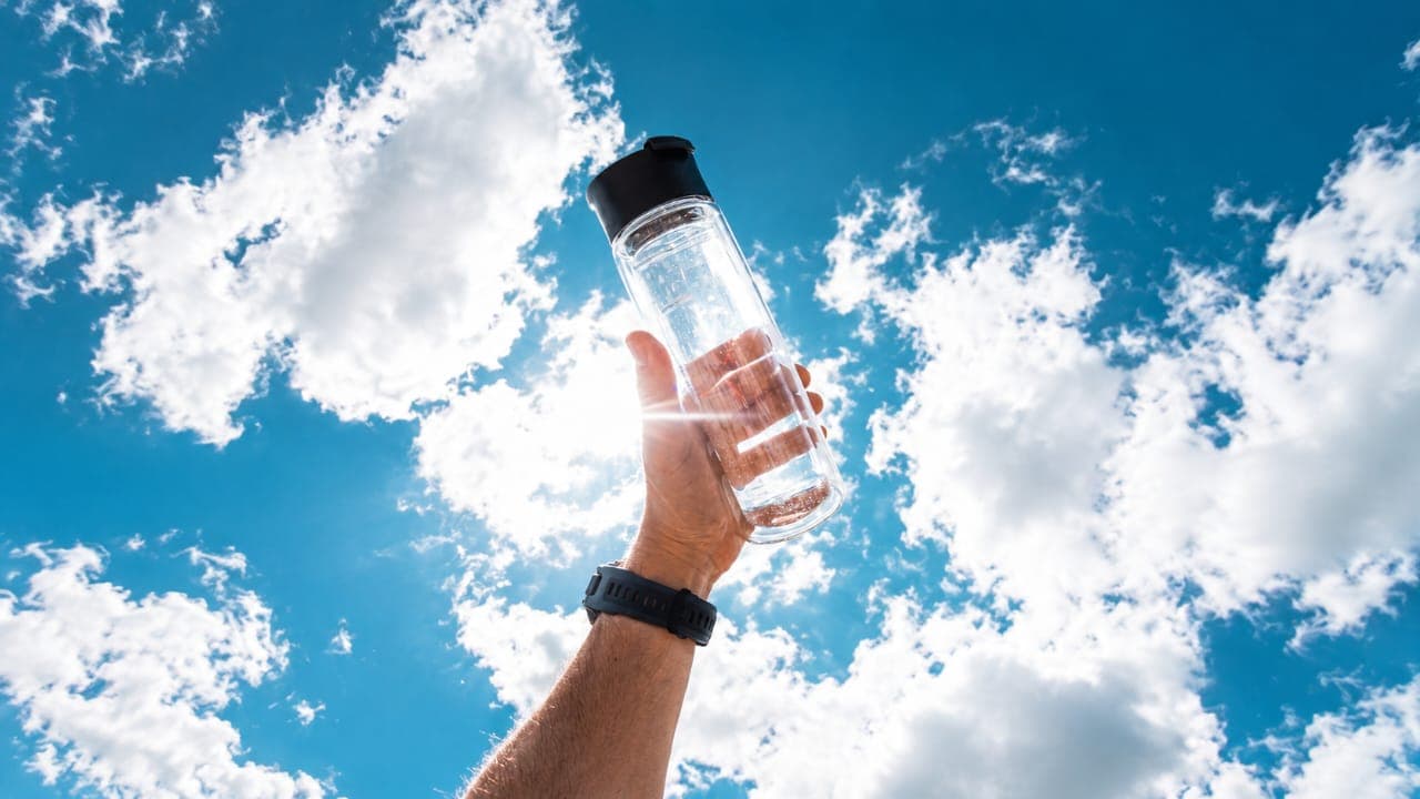 Water being poured from a glass bottle into a glass against a black background